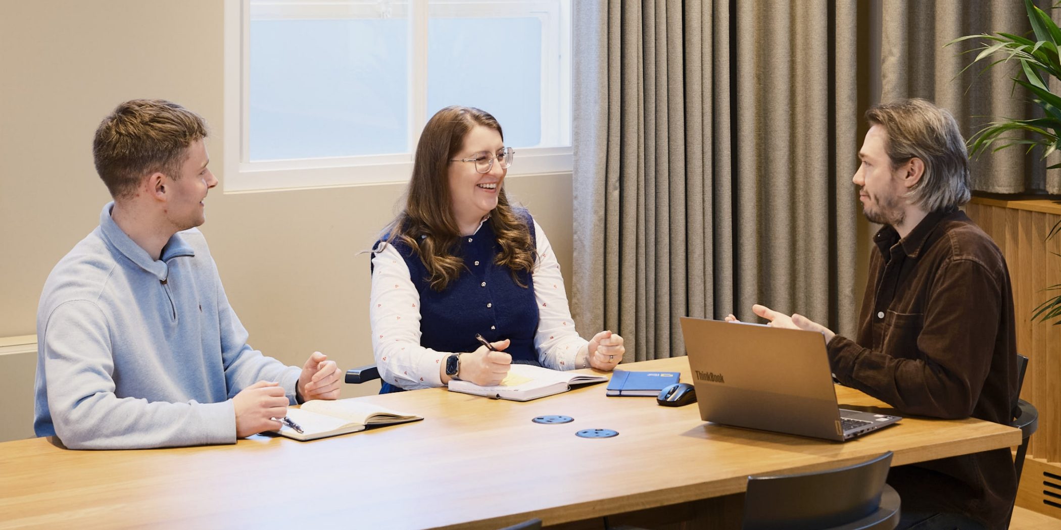 3 people sitting at a table having a meeting with a laptop