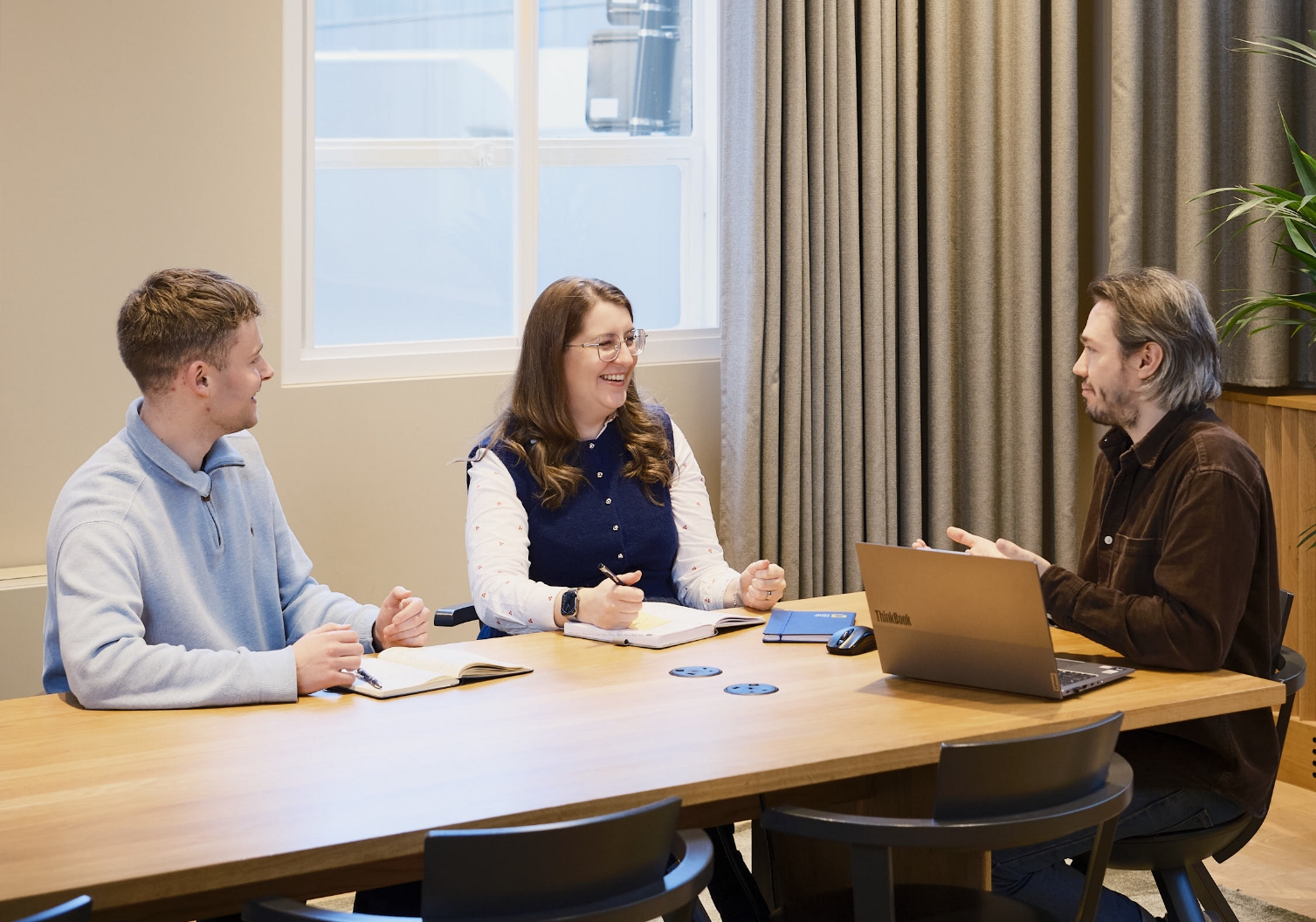 3 people sitting at a table having a meeting with a laptop