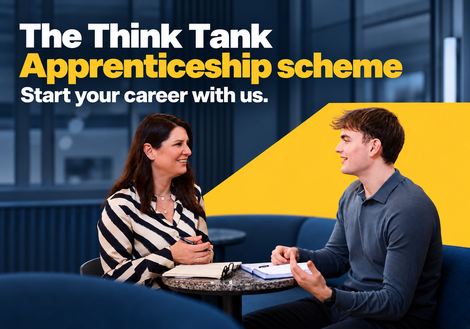 2 colleagues sitting at a table having a meeting. Apprenticeship scheme text over image.